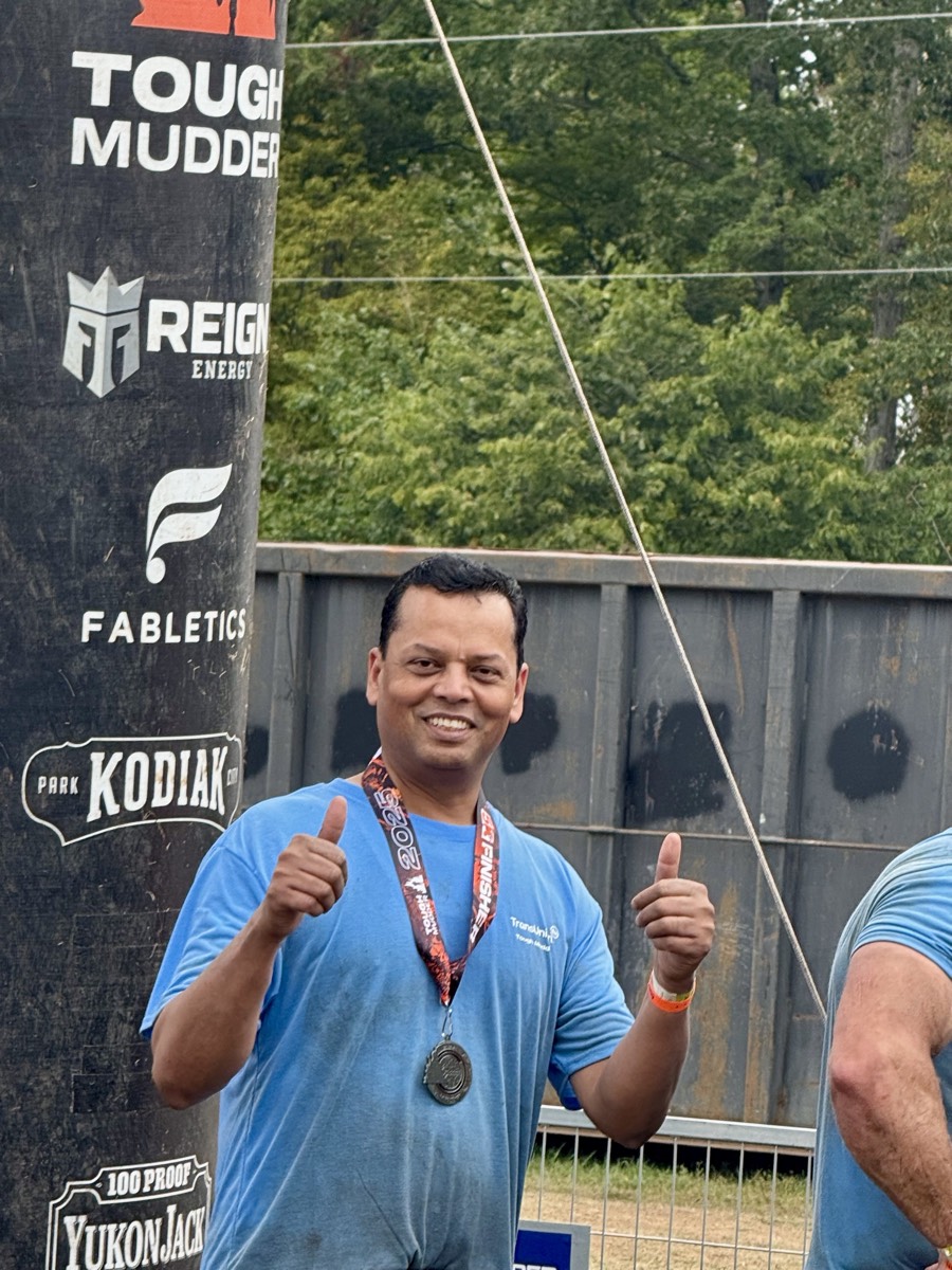 Arvind Choudhary smiling with two thumbs up, wearing a 2025 Tough Mudder finisher's medal at the finish line.